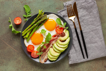Tasty breakfast. Fried eggs with green asparagus, fried bacon on black plate on wooden table. Top view