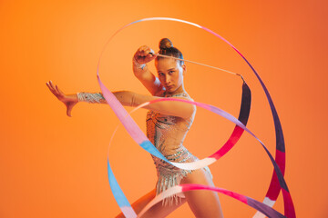 Young sportive girl, rhythmic gymnastics artist dancing isolated on orange color background....