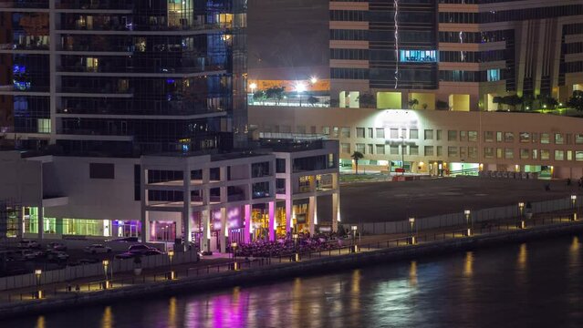 Cityscape of skyscrapers in Dubai Business Bay with water canal aerial night timelapse. Modern skyline with illuminated towers and caffee on a waterfront. A center of international business