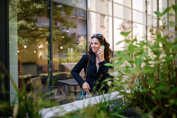 Happy woman calling on mobile phone and waiting outside the cafe in city.