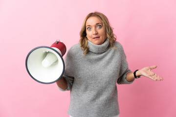 Middle aged blonde woman over isolated pink background holding a megaphone and with surprise facial...