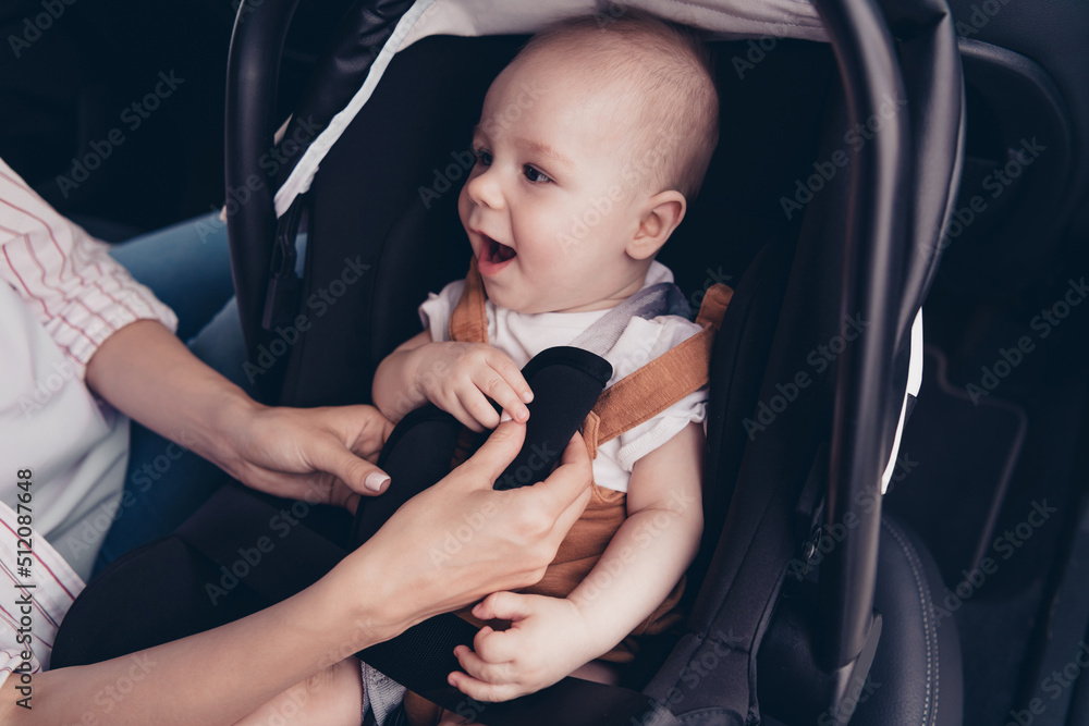 Wall mural Cropped photo of mother hands put help toddle sitting safety baby chair automobile salon inside