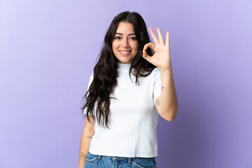 Fototapeta premium Young caucasian woman isolated on purple background showing ok sign with fingers