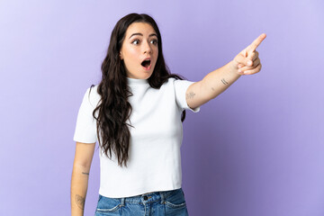 Young caucasian woman isolated on purple background pointing away