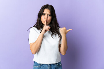 Young caucasian woman isolated on purple background pointing to the side and doing silence gesture