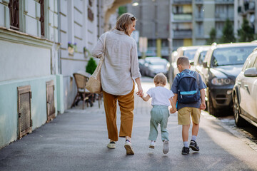 Young mother with zero waste shopping bag holding hands with her children and walking in city street street