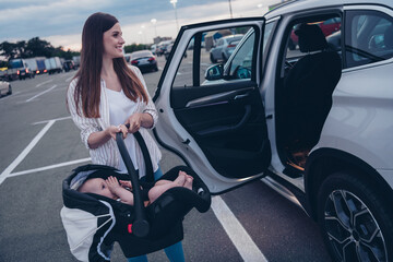 Photo of sweet cheerful mom small daughter wear casual outfits open door putting car seat inside...