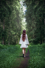 a young woman with long hair in a white dress walks along a path into the forest, an abyss concept, getting lost, danger