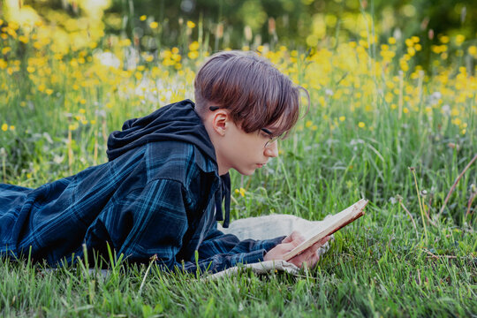 young man lies in the park on the grass and reads a book