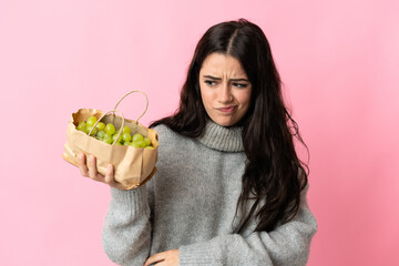 Young caucasian woman holding a grapes isolated on blue background with sad expression