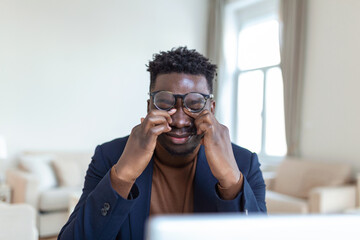 Tired African American businessman taking off glasses, exhausted employee massaging nose bridge, suffering from eye strain after long computer work, feeling pain, health problem concept