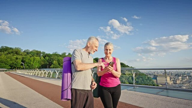 Elderly man and woman watch photos on smartphones walking