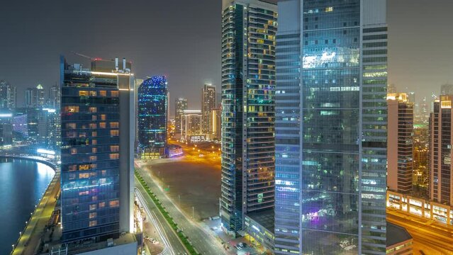 Cityscape of skyscrapers in Dubai downtown and Business Bay with water canal aerial night timelapse. Modern skyline with illuminated towers and waterfront. A center of international business