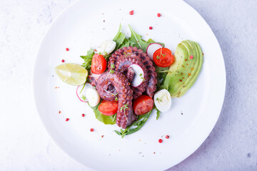 Warm salad with octopus, cherry tomatoes, avocado, arugula, quail eggs, radish and lime on a white plate. Traditional Mediterranean dish. Close-up, white background.