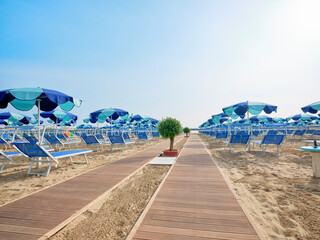 Boardwalk on the beach along a row of colorful umbrellas and sunbeds leading to the sea on a sunny...
