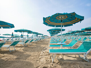 Boardwalk on the beach along a row of colorful umbrellas and sunbeds leading to the sea on a sunny...