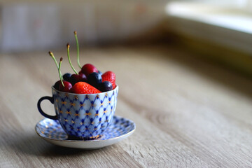 Vintage porcelain cup filled with strawberries, blueberries and cherries. Selective focus.