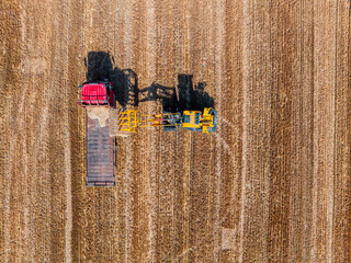 Agricultural tractor loads wheat straw on truck. Aerial view. agricultural machinery. Hay stacks...