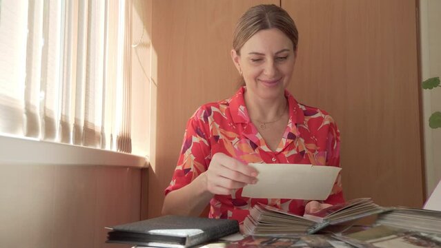 A young woman looks at photos in a photo album and remembers a pleasant vacation time. High quality 4k footage