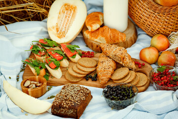 Picnic on the grain field. A natural snack, grain bread with salmon, berries and melon on a wooden board and a blanket in the fresh air.