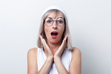 Shocked young woman in a white hat and glasses on a light background