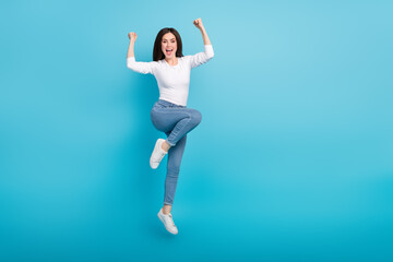 Fototapeta na wymiar Photo of funny lucky woman wear white shirt rising fists jumping high empty space isolated blue color background