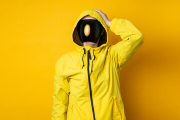 A young woman in a mask of cyberpunk goggles in a yellow jacket holds her head with her hand on a yellow background