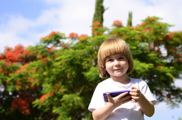 Portrait of a boy with a phone. Children and smartphone. Child in the garden, tree in bloom. Concept: conversation with parents, parental control, personal conversation, mobile communication