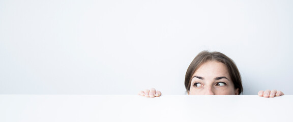 Young woman looking to the side looking out from under a white table against a white wall. Banner