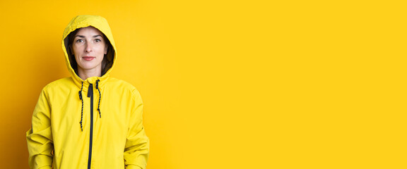 Young woman in a yellow hooded jacket on a yellow background. Banner