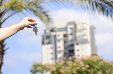 Close-up hand holding a key on the background of a beautiful high-rise building. Concept: buying an apartment, renting a house, real estate loan