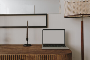 Laptop computer on wooden console with candle, floor lamp. Aesthetic elegant styled home living room interior design. Online store, blog, social media, shop branding template with blank copy space