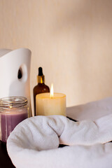 Skin and body care or spa attributes on a wooden table, massage oil, white towel, candles, aroma diffuser