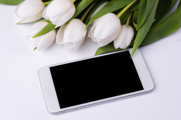 Bouquet of white tulips with blank screen mobile smartphone. Copy space for text.