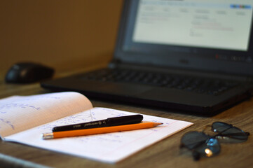 Open laptop on the desk with copybook and pen, working process