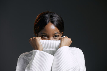 Serious african american woman hiding face behind collar of stylish warm knitted cozy winter sweater. Silence concept