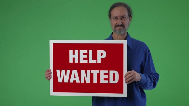 Closeup of man in blue shirt holding Help Wanted sign on solid green screen chroma key background.