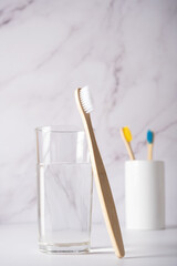 A bamboo toothbrush with white bristles next to a glass of clean water.