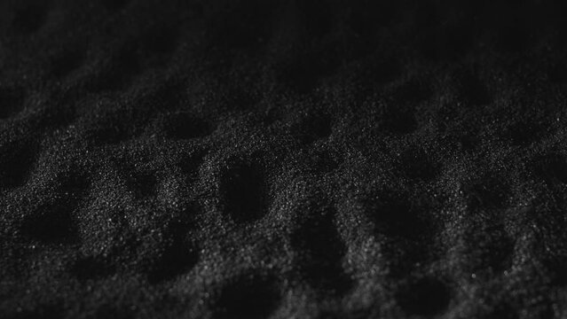 Black sand surface with dimples. Monochrome textured background of dark beach sand. Gunpowder, grained dust 