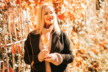 Beautiful blonde 35 years old in blac kcoat and beige sweater holds glass with autumn cocktail in...