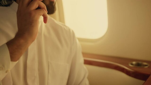 Arabian businessman talking phone on private jet. Closeup hand picking cellphone