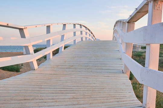 beautiful white wooden bridge on the embankment by the sea at sunset © Alexander