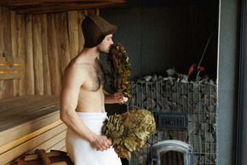 Attractive man sniffing a broom in the sauna