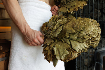 Man in a sauna holds a broom for a bath made of maple leaves