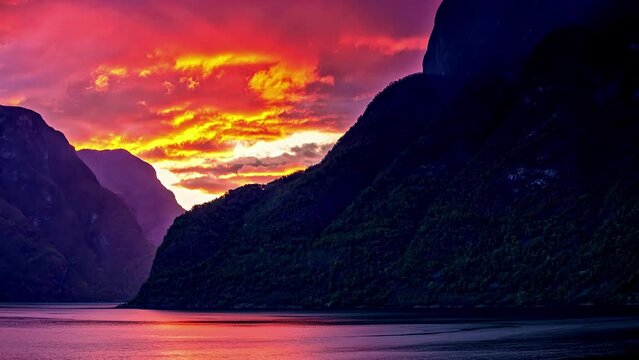 Timelapse shot of colorful clouds passing by over norwegian fjord water between mountains during sunset.