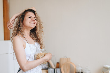 Young Wife in an Apron is Going to Cook Pasta. Woman Joyfully Laughs while holding jar of pasta in...