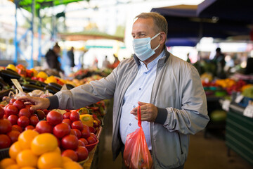 Man in face mask choosing tomatoes in greengrocery
