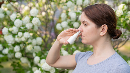 Fototapeta premium Caucasian woman uses a nasal spray while walking in the park.
