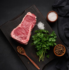 Fresh raw piece of beef meat, striploin steak on a black background, top view. Marbled piece of meat