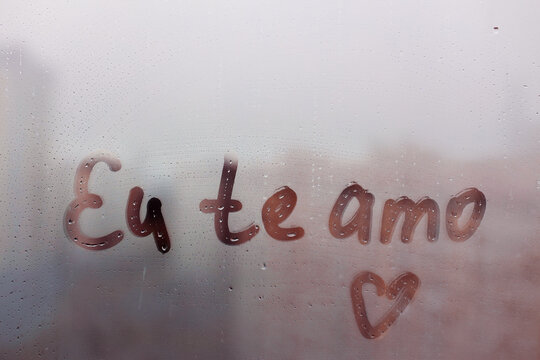 Lettering Portuguese text Eu te amo I love you in english and heart shape on sunset wet window